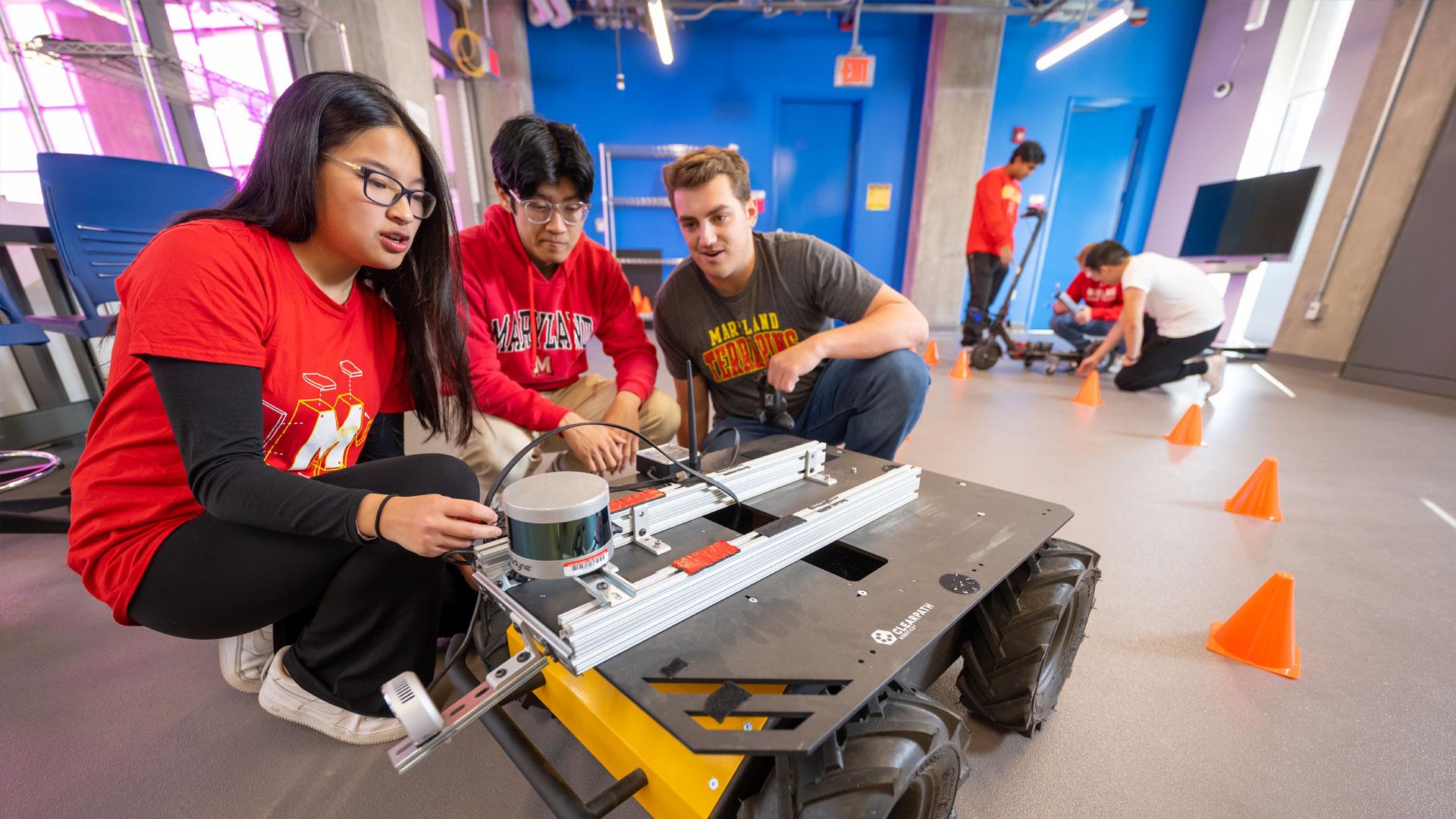 Students in a E.A. Fernandez IDEA factory lab talking to each other while surrounding a Clearpath HuskyA200 field robot.